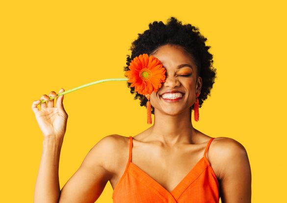 Smiling woman holding flower in front of eye